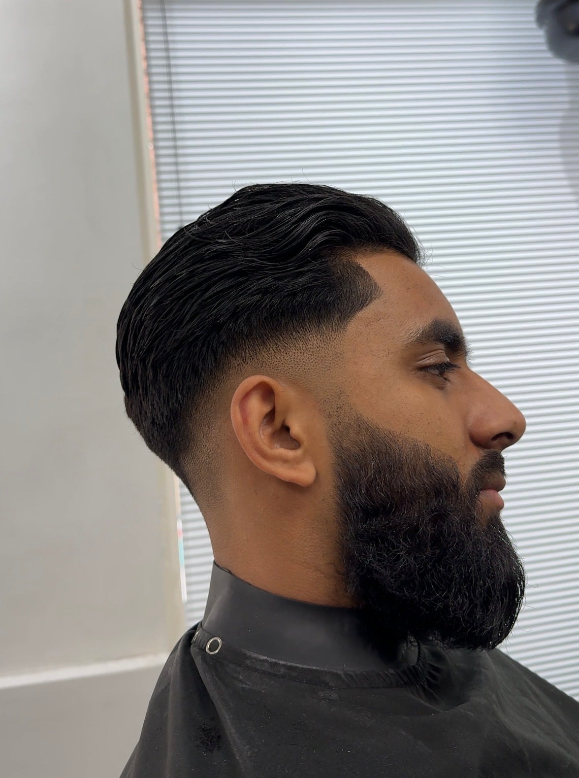 Zijprofiel van een klant met een drop fade, achterover gekamd haar en een volle baard