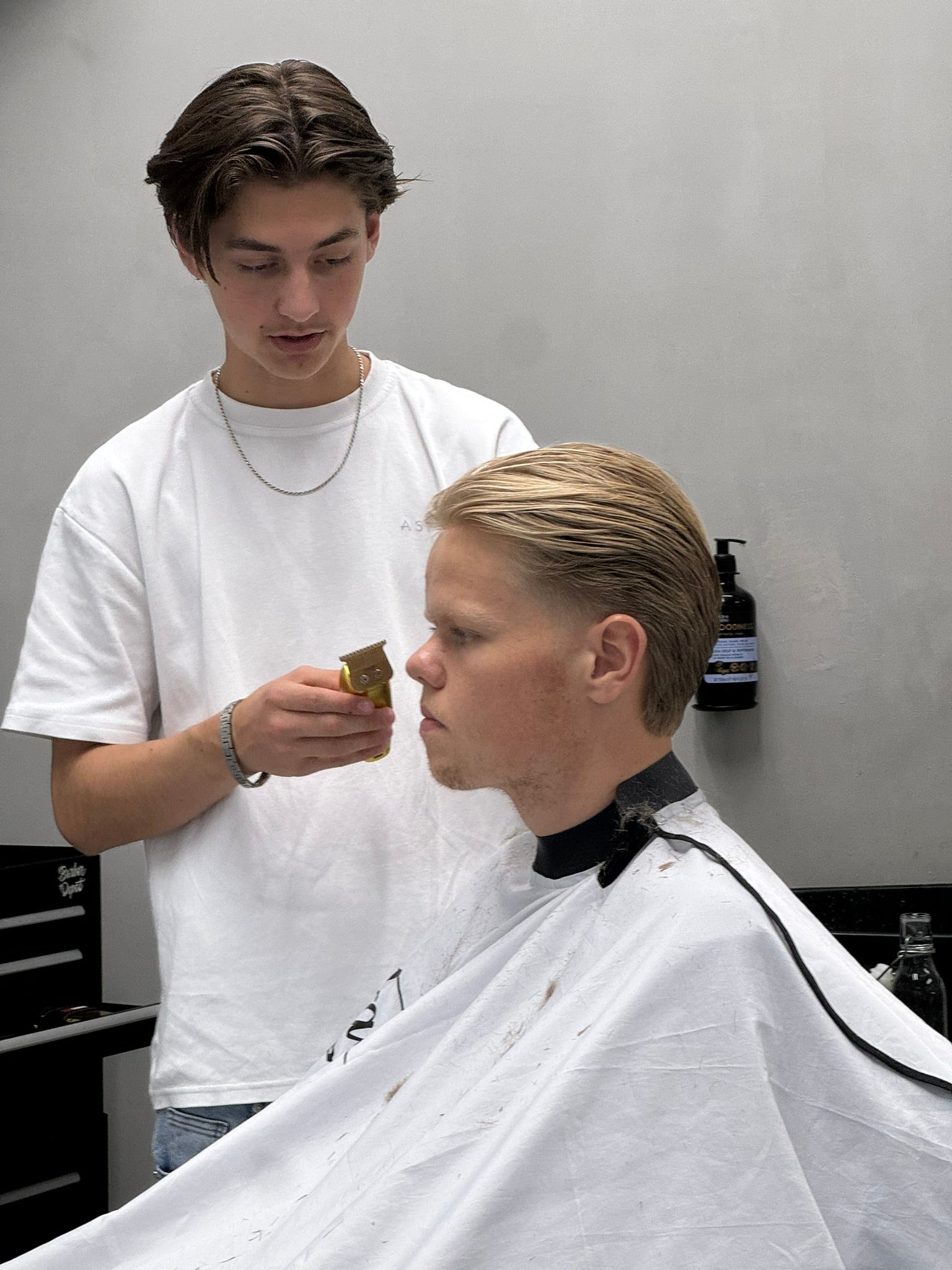 Een barber in een wit shirt bekijkt de coupe van een klant in een Fadeful-kaap
