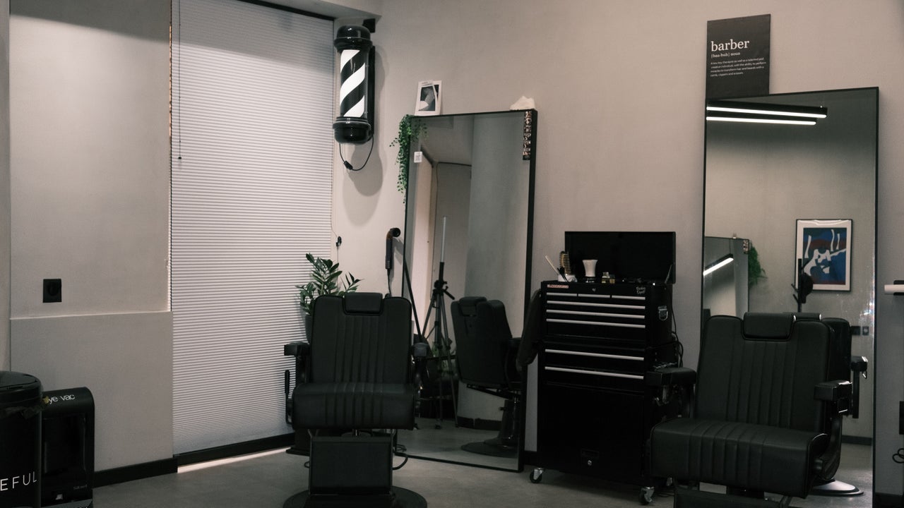 Zwarte barberstoelen voor grote spiegels, met een barberpaal aan de muur