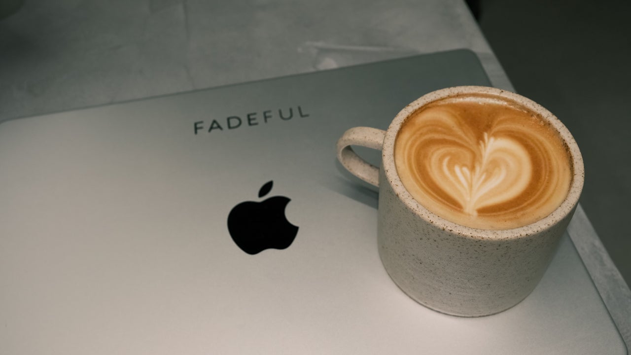 Een latte met een hart in het schuim op de balie, naast een iMac met FADEFUL erop